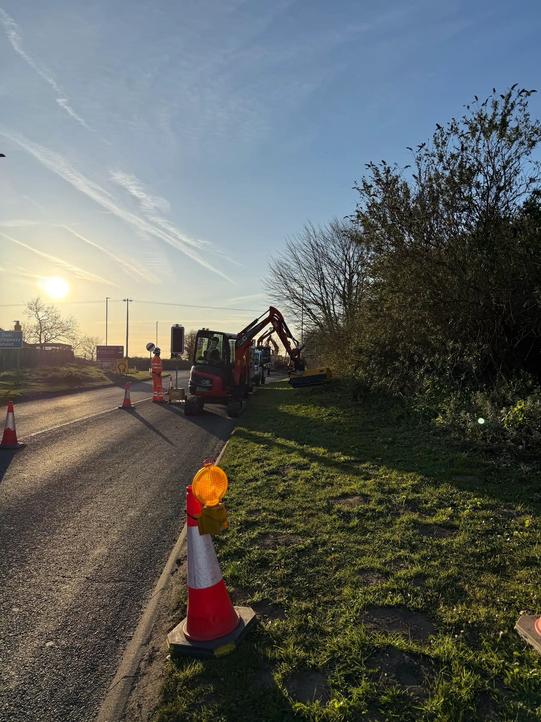 A GroundCore excavator clearing a roadside hedge and boundary at sunrise in Caister